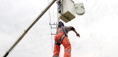 Worker suspended below cherry picker from fall protection system 
